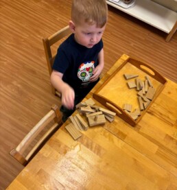 Lyonsgate Montessori School Toddler student building sculptures with wooden blocks to develop fine motor skills and creativity.