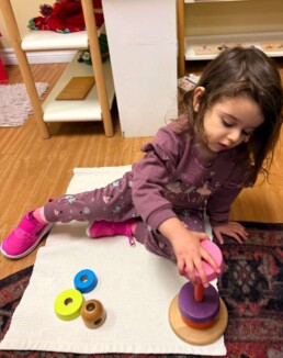 Lyonsgate Montessori School Toddler student building motor control skills and being introduced to the sensorial understanding of relative sizes.