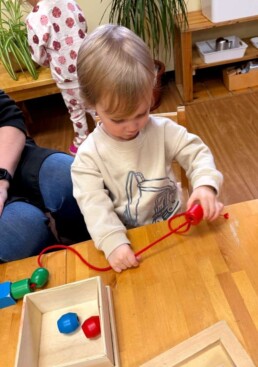 Lyonsgate Montessori School Toddler student building motor skills and concentration with a bead threading activity.