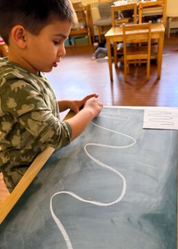 Lyonsgate Montessori School Casa student engaged in some preparation for writing work by recreating shapes and patterns on a chalkboard.
