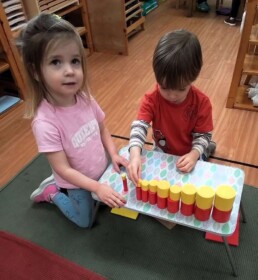 Lyonsgate Montessori School Casa students working together with the Montessori Knobless Cylinders material that helps develop a sense of comparative size and volume, and builds fine motor skills and focus.