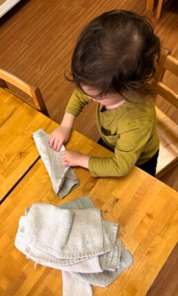 Lyonsgate Montessori School Toddler student folding the cloths to put away for the classroom to use.