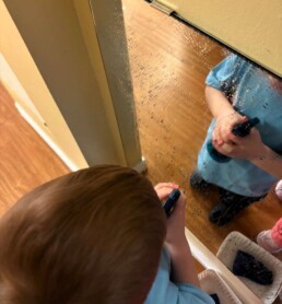 Lyonsgate Montessori School Toddler student taking care of his environment by washing a mirror and keeping it clean!