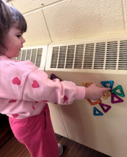 Lyonsgate Montessori School Toddler student making a flower out of magnetic blocks. She is bringing real life into creative learning.