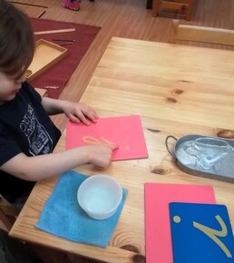 Lyonsgate Montessori School Casa student learning cursive letter shapes with the Montessori Sandpaper Letters material.