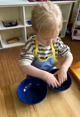 Lyonsgate Montessori School Casa student engaged in a Montessori squeezing a sponge activity that is both an introduction to science and builds the hand strength needed for later writing and manipulative work.