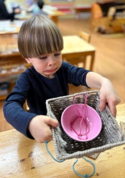 Lyonsgate Montessori School Casa student working hard to set up the weaving basket.