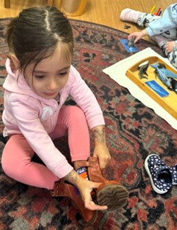 Lyonsgate Montessori School Toddler student demonstrating ever-growing independence by putting on and taking off her own shoes and boots.