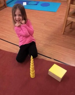Lyonsgate Montessori School Casa student excited about her successful work with the Montessori Knobless Cylinders material, a way to develop visual discrimination of comparative sizes.