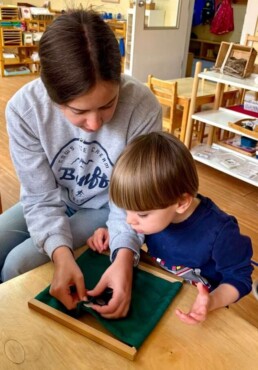Lyonsgate Montessori School Casa student receiving a presentation of a Montessori Dressing Frame to learn how to build independence.