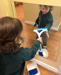 Lyonsgate Montessori School Toddler student taking care of the classroom environment by cleaning the mirror, while building focus and motor skills.