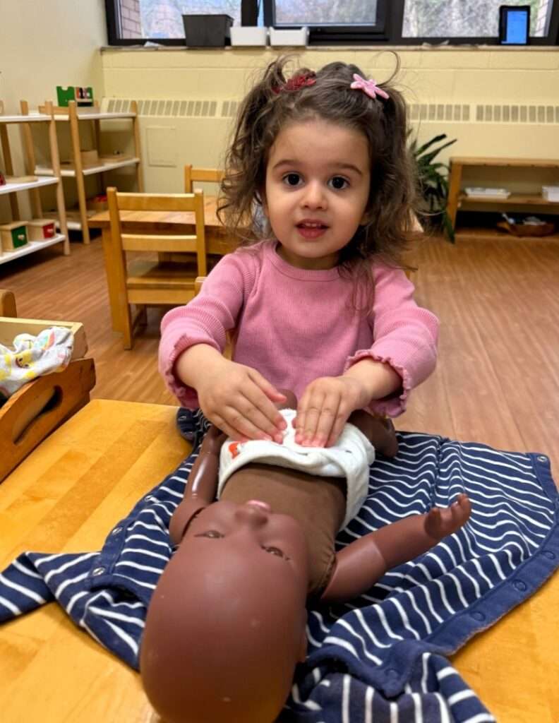 Lyonsgate Montessori School Toddler student practicing changing a diaper so she can be a big help at home.