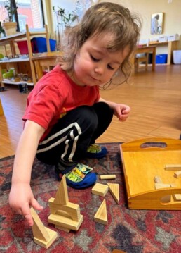 Lyonsgate Montessori School Toddler student working with wooden blocks for creative fun while building motor skills and focus through a tactile and visual introduction to geometric shapes.