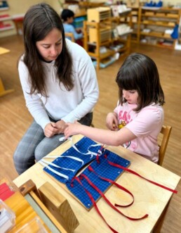 Lyonsgate Montessori School Casa student receiving a presentation of the Montessori Bow Frame to learn how to tie bows and build confidence and independence.