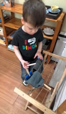 Lyonsgate Montessori School Casa student hanging classroom cloths to dry, and using clothes pins to build fine motor skills and hand and finger strength and dexterity in preparation for later writing work.