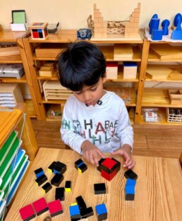 Lyonsgate Montessori School Casa student building the Montessori Trinomial Cube material puzzle outside of its container box to add an extra challenge to the activity.