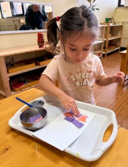 Lyonsgate Montessori School Toddler student creating pasting art, an activity builds motor control skills and introduces geometry vocabulary.