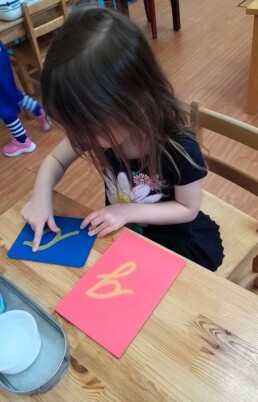 Lyonsgate Montessori School Casa student preparing to enter the world of writing by working with the Montessori Sandpaper Letters material.