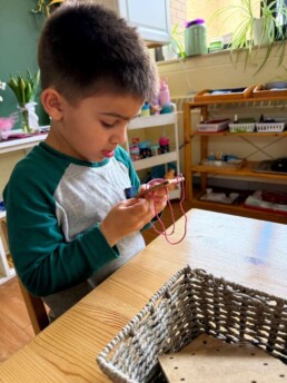 Lyonsgate Montessori School Casa student working at a sewing activity, which is a practical life skill and great way to develop fine motor skills and concentration.