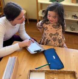 Lyonsgate Montessori School Casa student working with her Montessori guide to develop a survey, which is vocabulary-building social interaction experience activity.