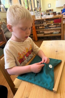 Lyonsgate Montessori School Casa student building independence with the Montessori Button Dressing Frame material.