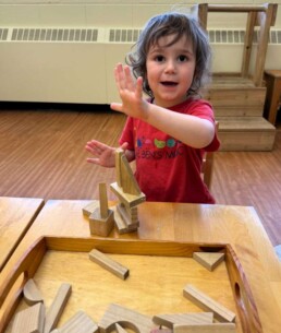 Lyonsgate Montessori School Toddler student proudly showing off his detailed block castle that he created.