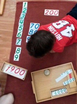 Lyonsgate Montessori School Casa student setting up his work with the Montessori Large Number Cards material.