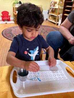 Lyonsgate Montessori School Toddler student developing hand-eye and fine motor skills by practicing painting in the dots.