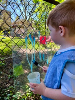 Lyonsgate Montessori School Toddler student enjoying outdoor fun while he helps to create a painting.