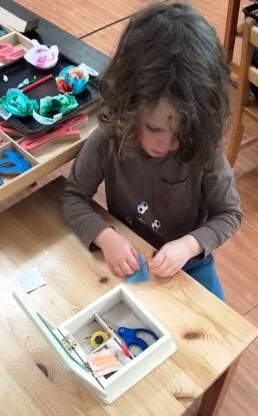 Lyonsgate Montessori School Casa student building fine motor skills, concentration, and a practical life skill by learning to sew on a button.