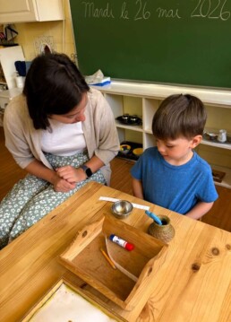 Lyonsgate Montessori School Casa student receiving a presentation of the Montessori Cutting Snippets activity that teaches the practical skill of using scissors while building motor skills and concentration.
