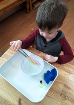 Lyonsgate Montessori School Casa student learning to use a whisk to create soapy, bubbly water for classroom cleaning use while developing motor and practical life skills, and concentration.