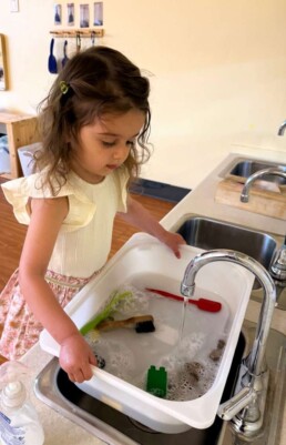 Lyonsgate Montessori School Toddler student preparing sensory bins for her class that they will use to scrub materials.